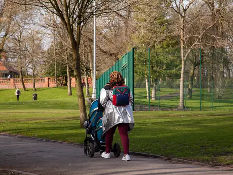A woman walking with a stroller through a sunny park