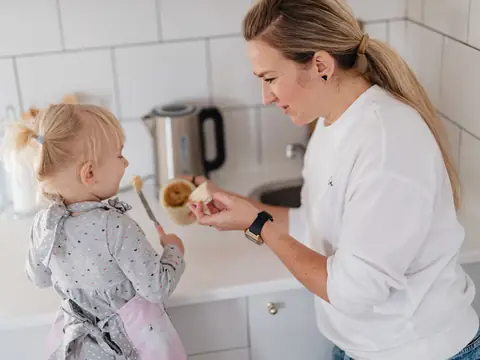 A mother sharing a spoonful of dessert with her small daughter in the kitchen
