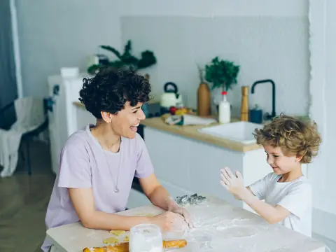 A mother laughing with her son while they bake at a kitchen table
