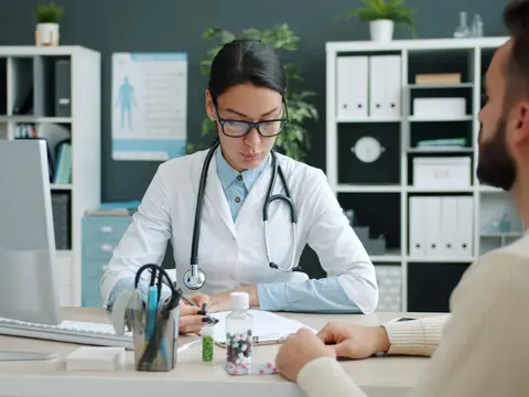A doctor taking notes across a desk during a consultation in a bright office
